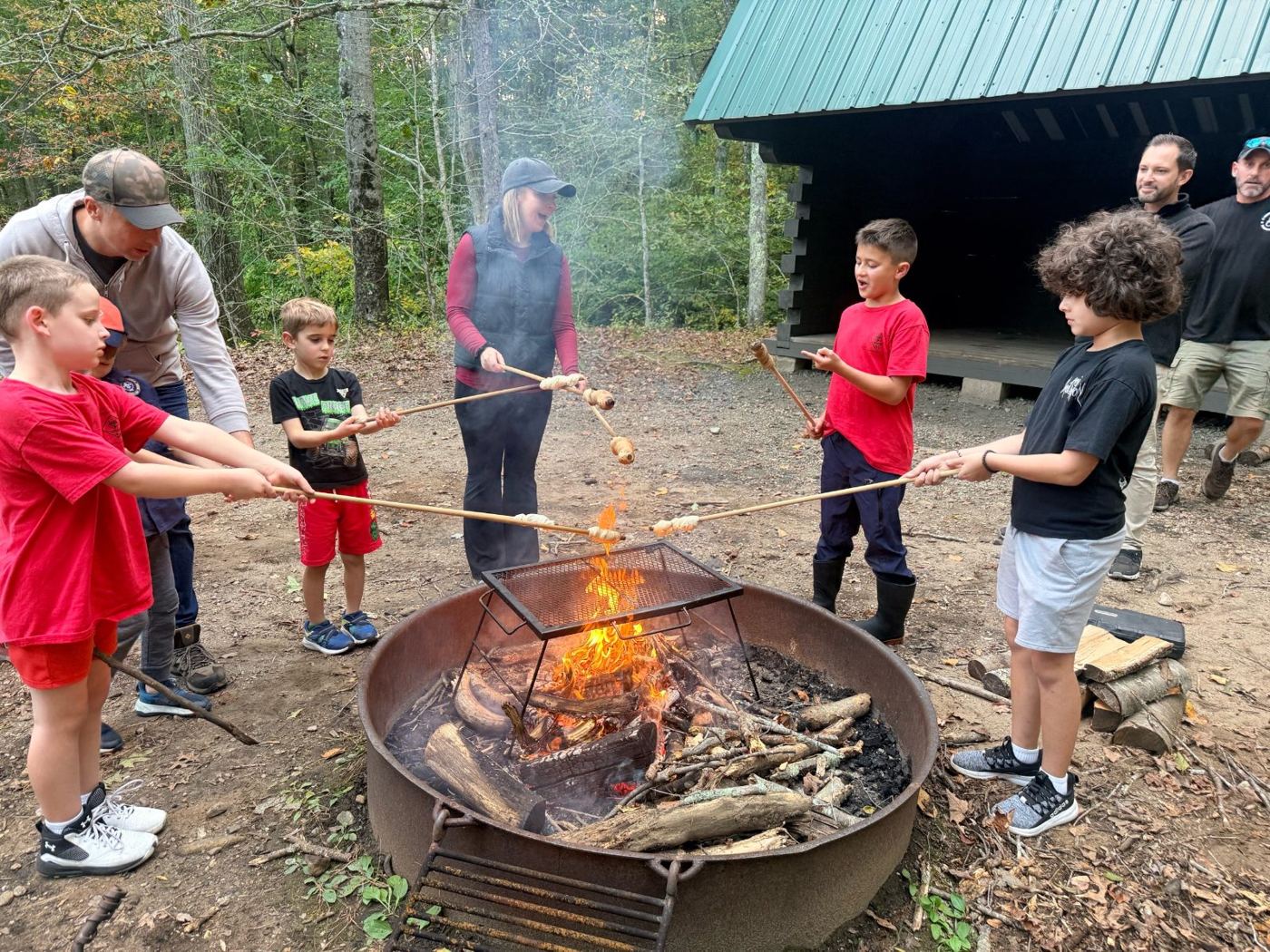 Scouts and parents roasting hot dogs over a campfire