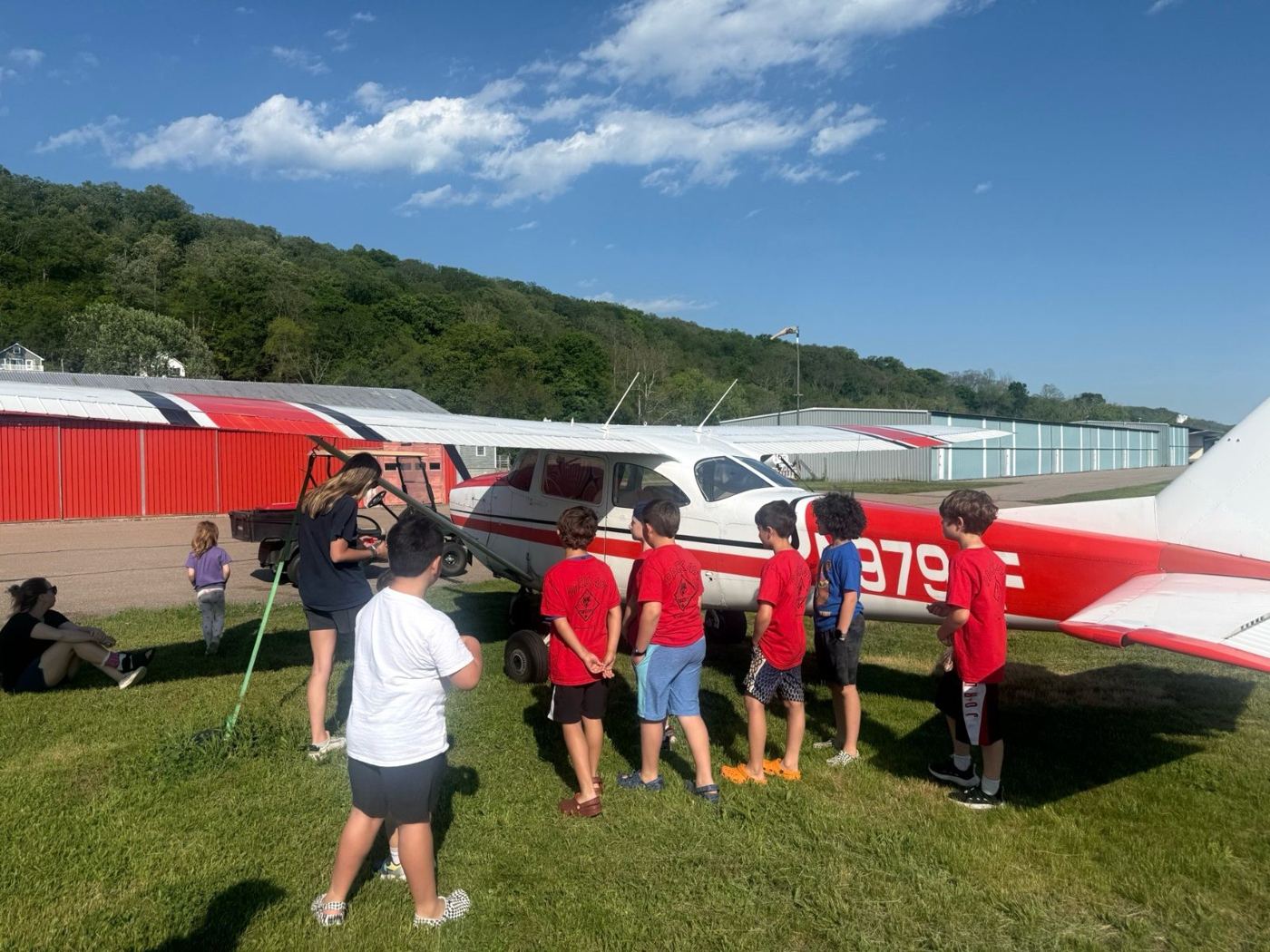 Cub Scouts looking at a red and white airplane on the grass