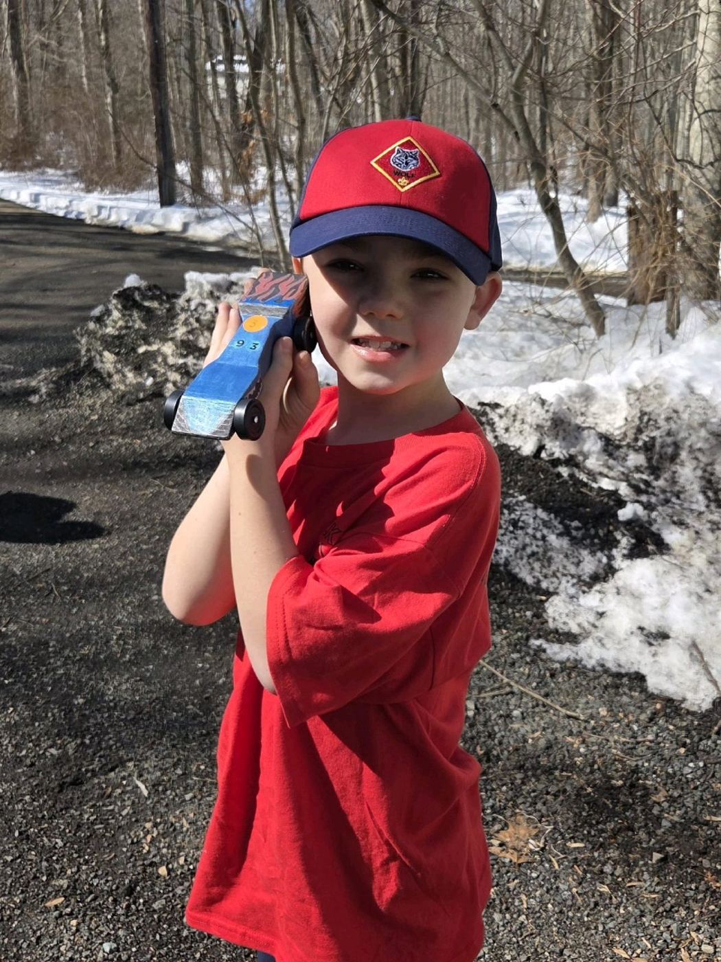A Cub Scout holding up his blue Pinewood Derby car